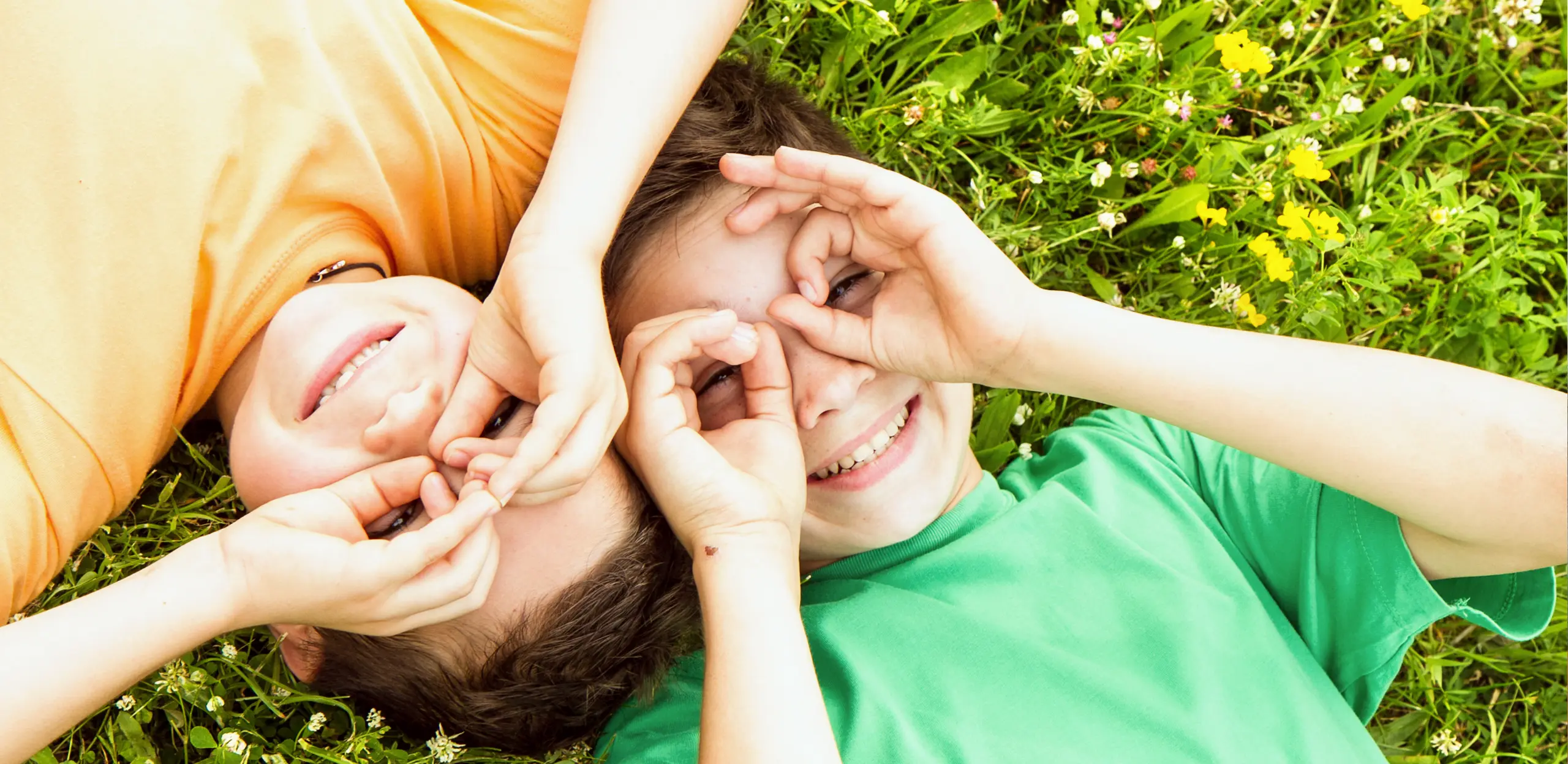 Deux enfants souriants couchés dans l'herbe — audition amiable de l'enfant, Londono Counseling Montréal